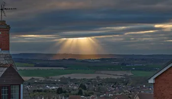 Gods rays on a cloudy spring evening over a solar farm as seen from houses.jpg